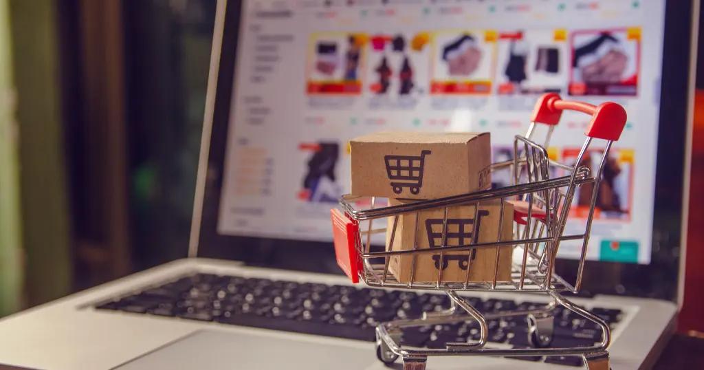 Tiny shopping cart with colorful bags on a laptop keyboard, symbolizing Shopify Development Services for online stores.