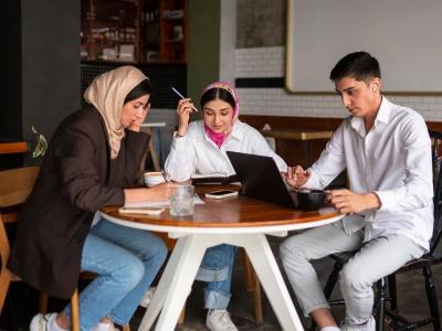 Three young people collaborating at a table, working on a laptop and taking notes. Relevant to the topic 'UK Visa From Pakistan'.