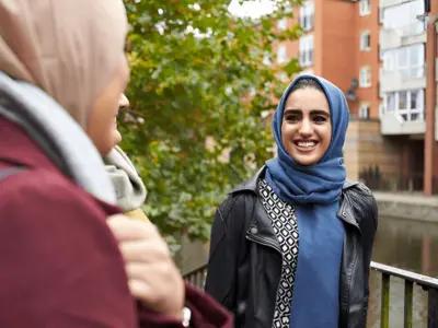Two women in hijabs smiling and chatting outdoors. UK Visit Visa from Pakistan enables cultural connections and travel.