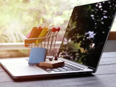 Mini shopping cart with boxes in front of a laptop screen showing products — Shopify Development Services visual concept.