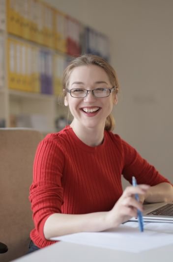 A smiling professional woman in a red sweater at her desk, next to a digital customer satisfaction rating screen, symbolizing quality service and positive feedback.